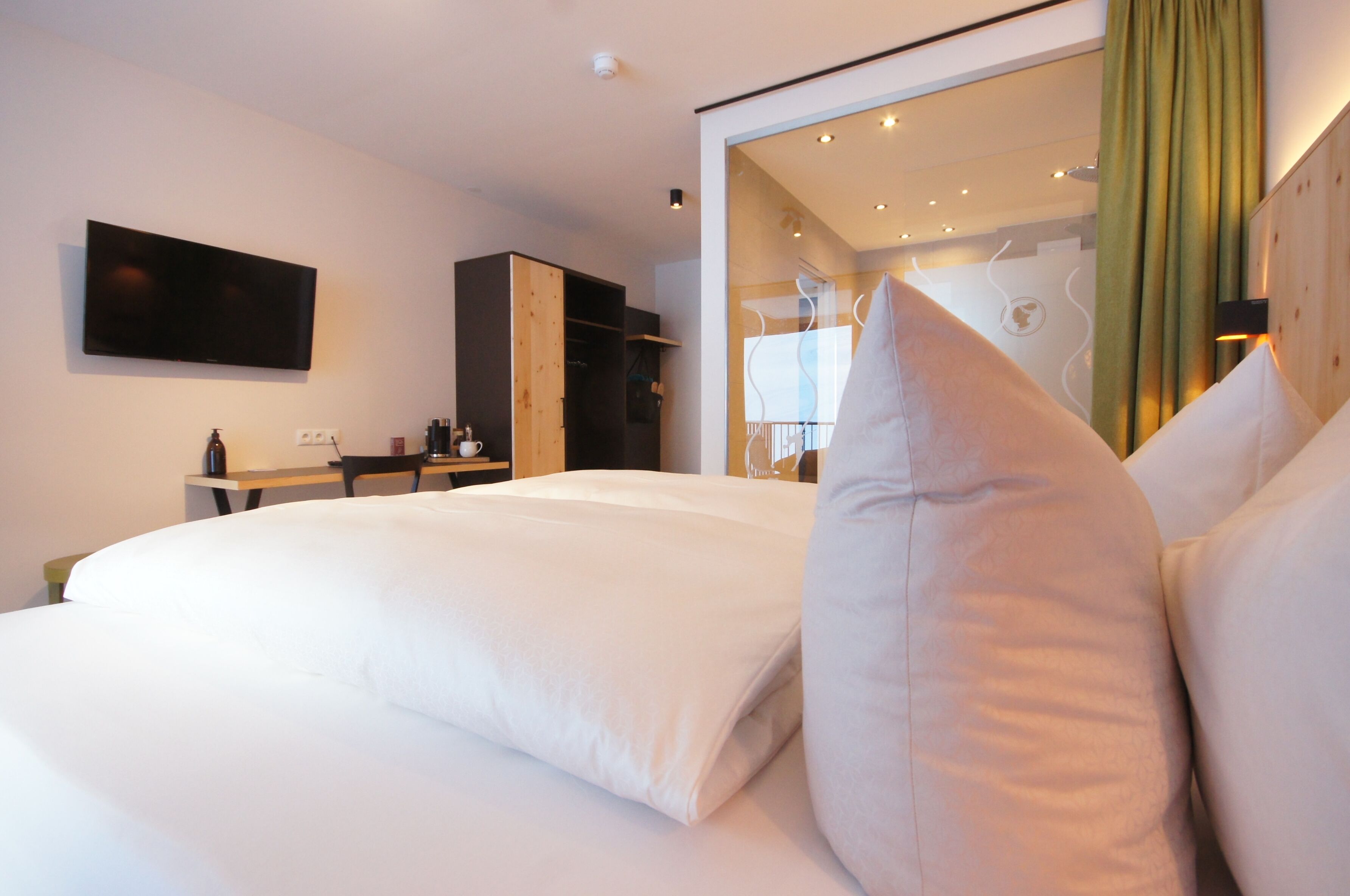 A hotel room with a large bed, a desk, and a wardrobe.