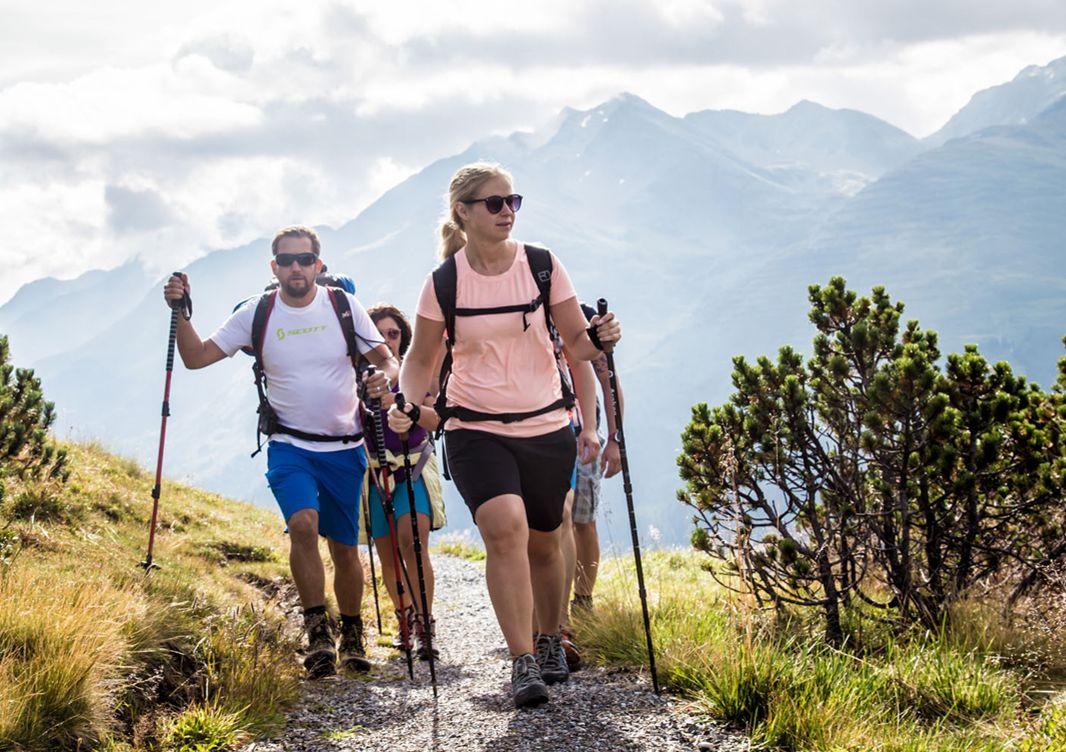 Un groupe de randonneurs sur un sentier de montagne, avec un ciel dégagé et des montagnes lointaines en arrière-plan.