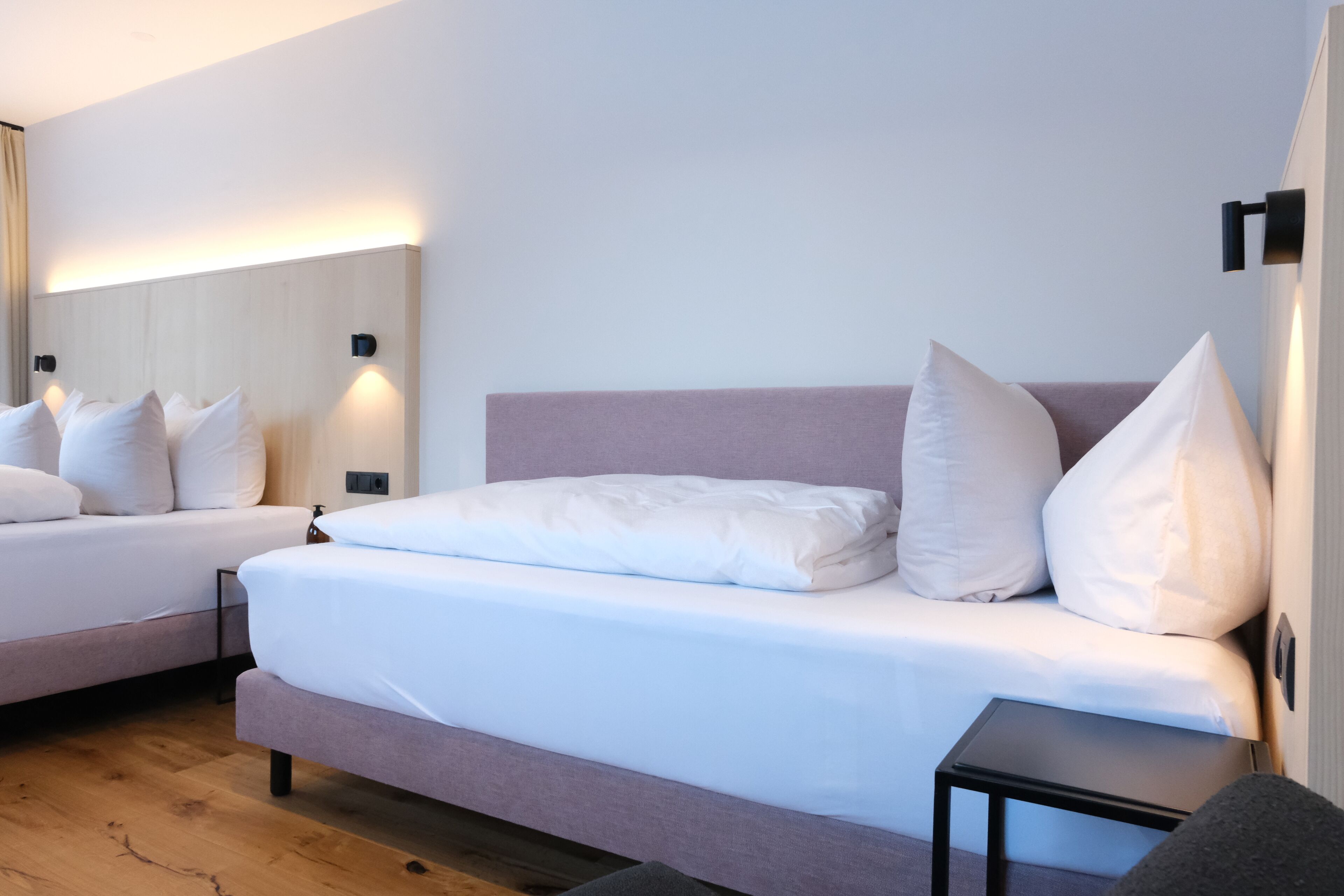 A modern hotel room with two beds, a small side table, and a large mirror.