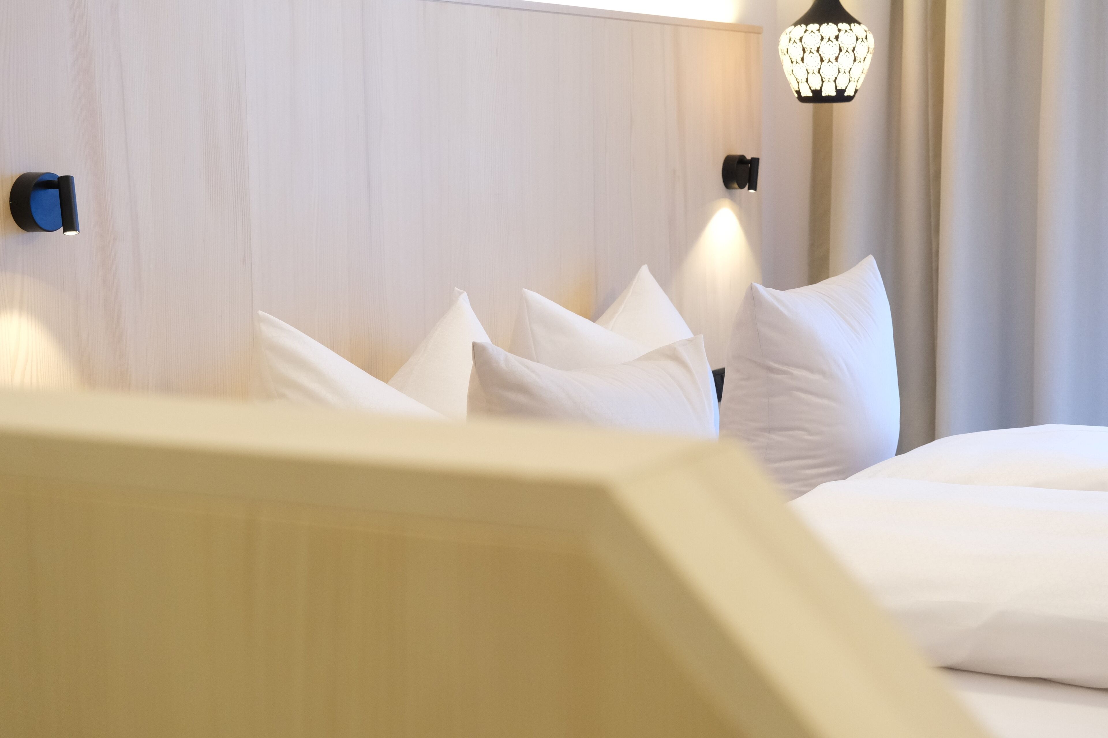 A hotel room with a wooden headboard, white bedding, and two wall-mounted light fixtures.
