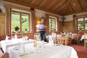 A dining area with wooden beams and large windows overlooking a green landscape. Tables are set with white tablecloths and silverware. - Hotel die Arlbergerin - Adults Friendly (Sankt Anton am Arlberg)