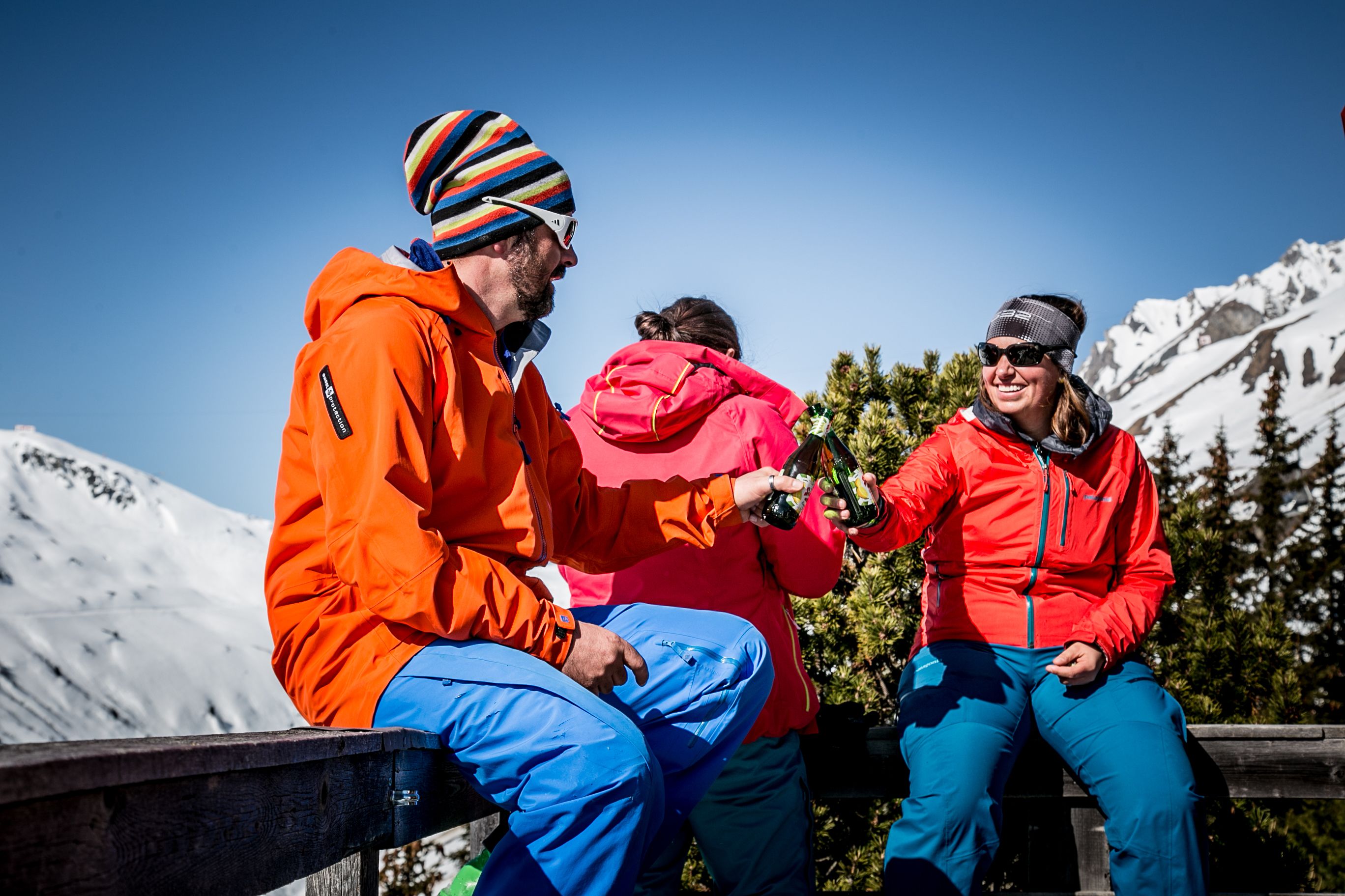 Three people sitting on a wooden bench in a mountainous area.