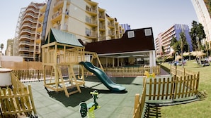 A playground with a slide and climbing structures, surrounded by a wooden fence. - Hotel Monarque Cendrillón (Fuengirola)