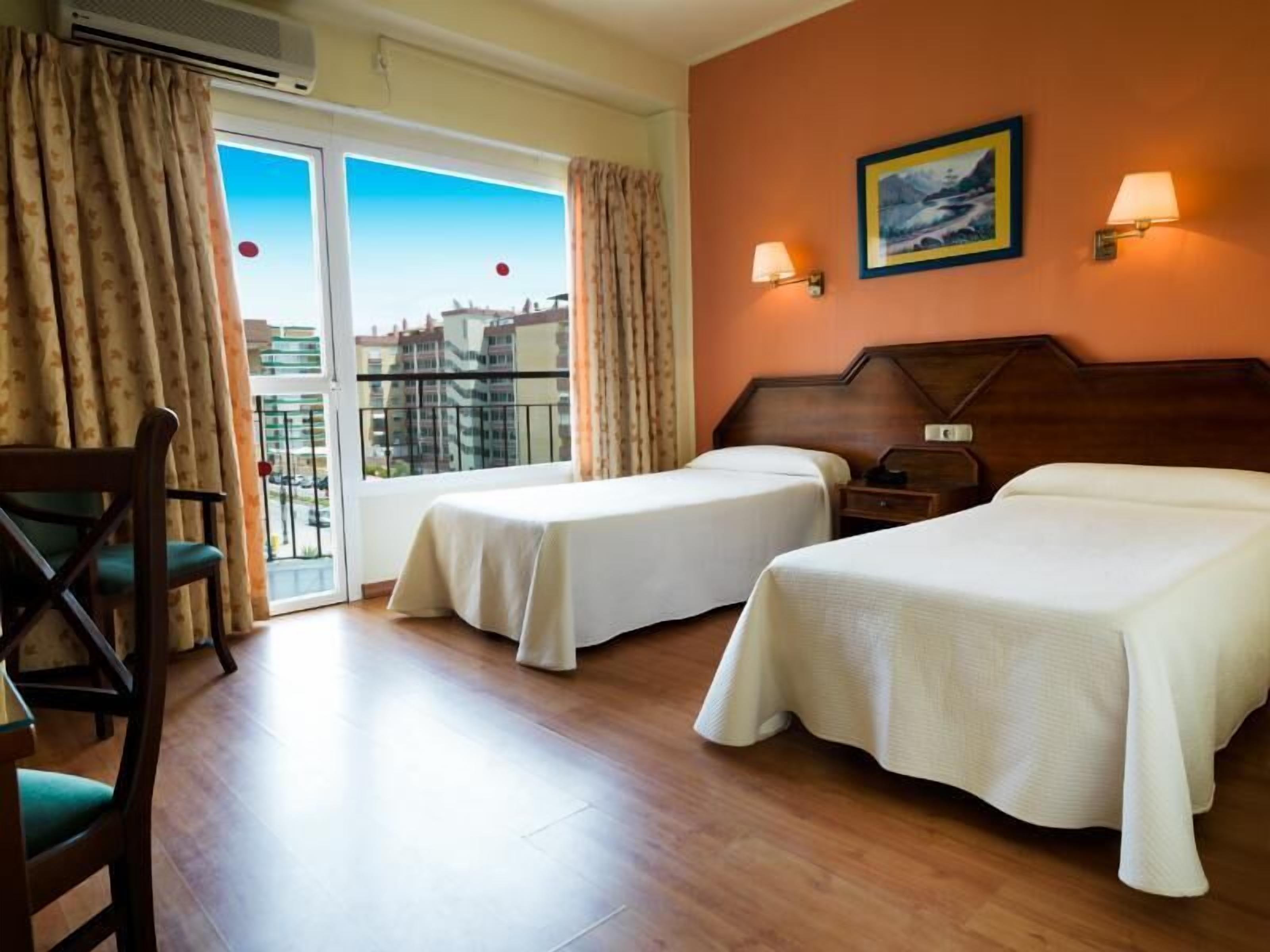 Une chambre d’hôtel avec deux lits, une chaise, une table, une table de chevet et un tableau au mur.