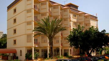 Un hotel de varios pisos con balcones, una palmera y un estacionamiento con coches.