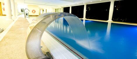 Una piscina con fuente, un sendero empedrado y vistas al cielo nocturno a través de amplias ventanas.