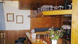 Zona de bar con taburetes, una barra con un jarrón de flores y estantes con copas y botellas.