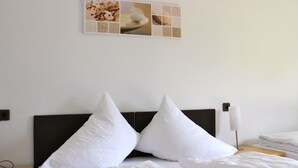 Una cama bien tendida con sábanas y dos almohadas blancas, una mesita de noche con una lámpara, y un cuadro colgado en la pared de postres.
