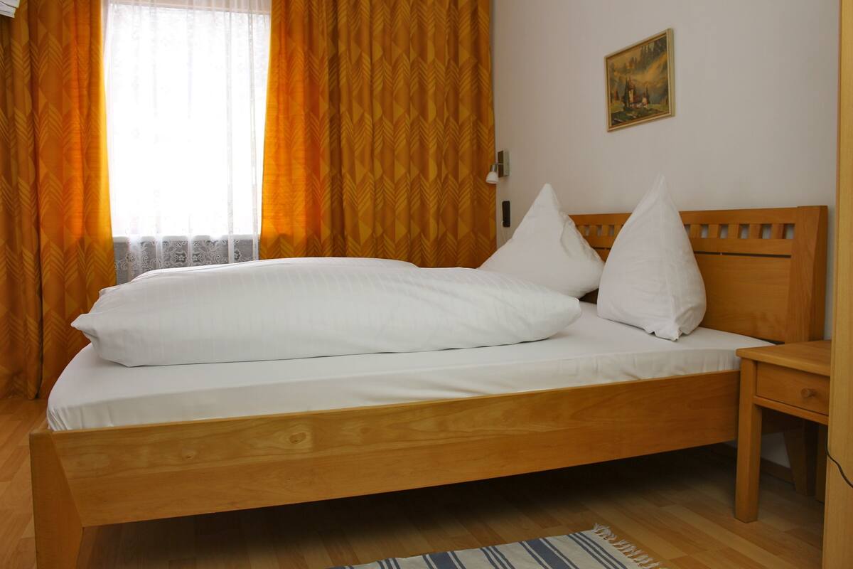 A wooden bed with white bedding, a nightstand, and a painting on the wall.