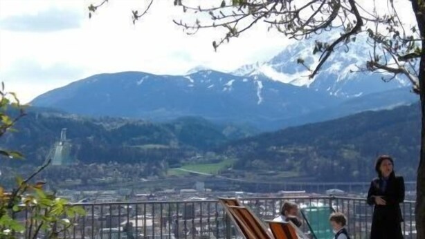 Un balcón con sillas y mesas que da a un paisaje montañoso con un pueblo lejano.