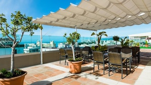 A terrace with outdoor seating, potted plants, and a view of the city and sea. - Hotel Monarque El Rodeo (Marbella)