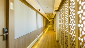 A hotel corridor with wooden paneling, a modern elevator, and a decorative wall with cut-out patterns. - Hotel Monarque El Rodeo (Marbella)