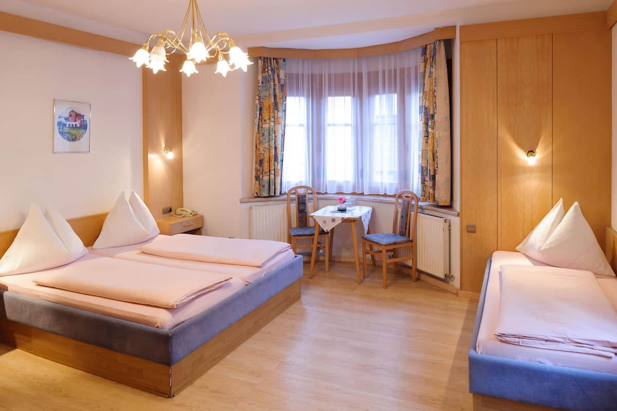 A hotel room with two beds, a dining table, chairs, a chandelier, and a window with curtains.