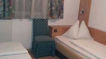 Habitación de hotel con dos camas, un taburete pequeño, una ventana con cortinas estampadas y un cabecero de madera.