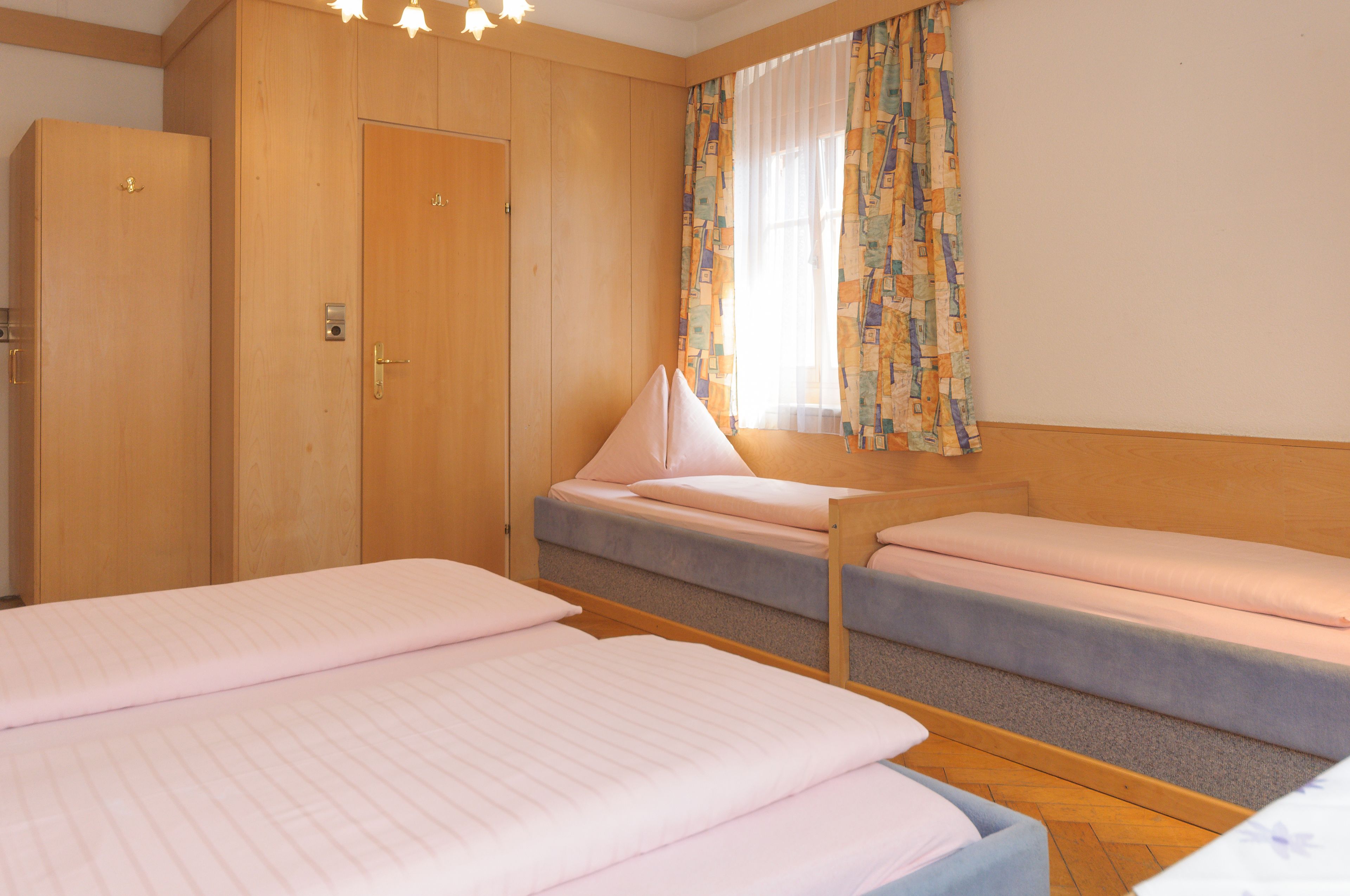 A room with two single beds, a wooden wardrobe, and a window with patterned curtains.
