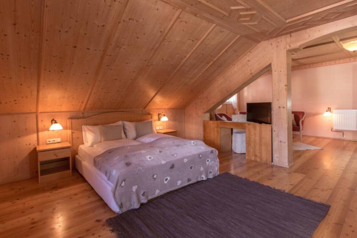 Un dormitorio acogedor en el ático, con techo de madera, una cama con manta estampada, lámparas de noche y un televisor.
