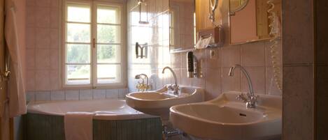 A bathroom with a bathtub, two sinks, a window, and a mirror.