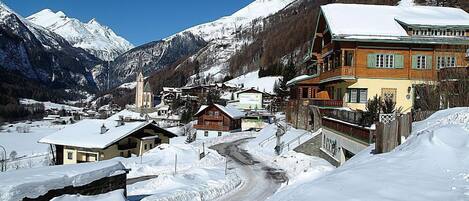 Un pueblo cubierto de nieve con casas de madera tradicionales, una iglesia y un edificio destacado con un balcón.