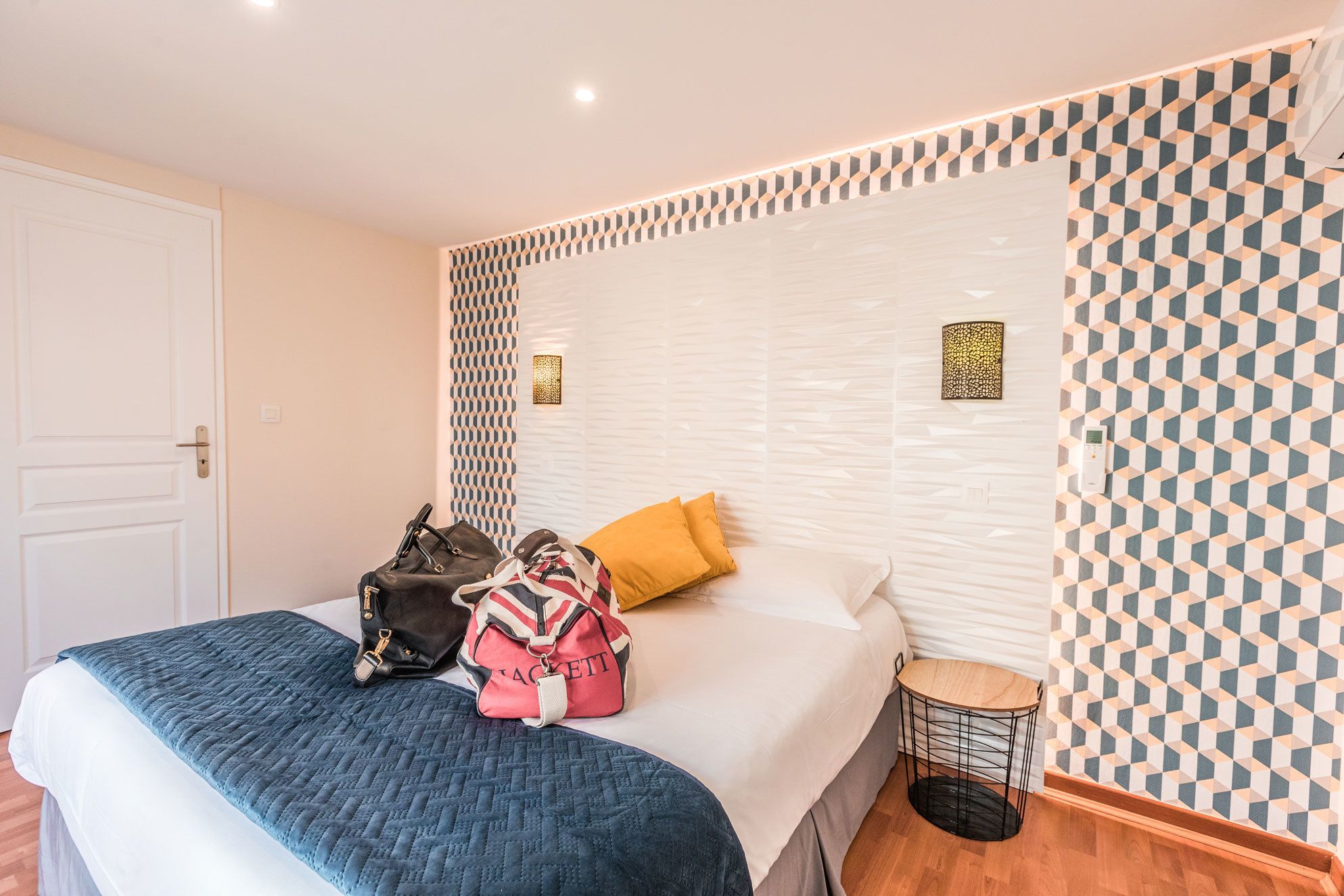 Una camera d'albergo con un letto, un comodino, una lampada e una parete decorata.