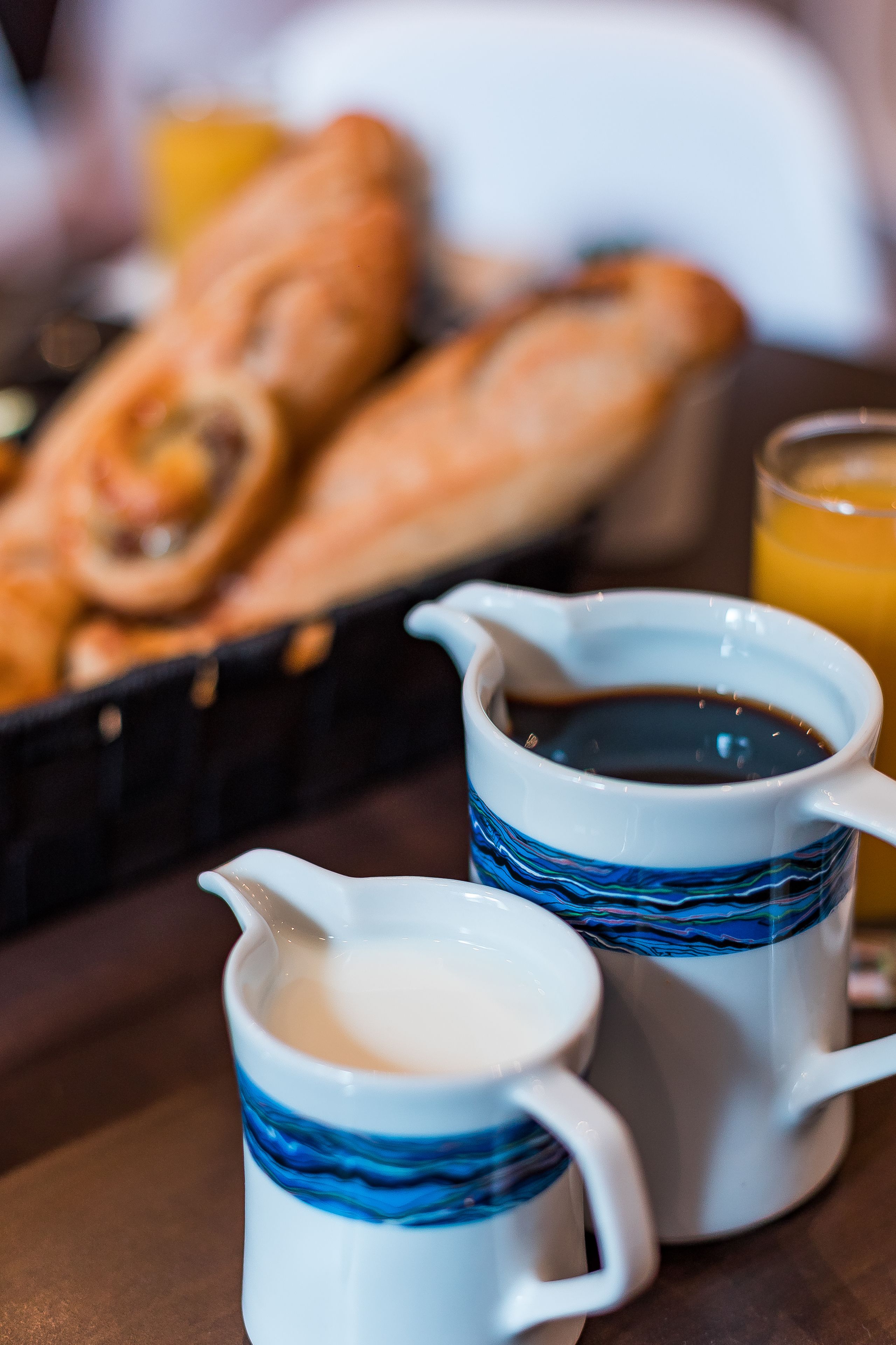 A breakfast setting with croissants, a coffee pot, and a glass of orange juice.
