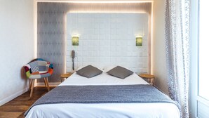 Une chambre d’hôtel moderne avec un grand lit, un fauteuil à motifs, deux lampes de chevet et un rideau à motifs.