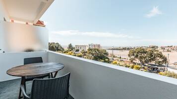 A balcony with a table and chairs, overlooking a cityscape with buildings and trees.