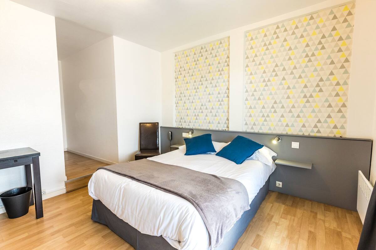 Quarto de hotel moderno com cama, mesas de cabeceira e parede estampada.