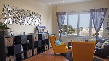 Un salon moderne avec un meuble de rangement noir pour les appareils électroniques, des fauteuils jaunes et une vue sur l’extérieur grâce à de grandes fenêtres.