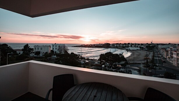 Un balcon offrant une vue sur la mer et les bâtiments au coucher du soleil.