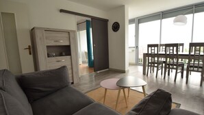 A modern living room with a grey sofa, a small round table, and a dining area with chairs. - Appart Hotel Beau Rivage (Royan)