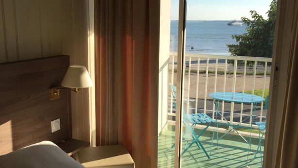 A hotel room with a bed, a nightstand, a lamp, a window with a view of the sea and a balcony with outdoor furniture. - Appart Hotel Beau Rivage (Royan)