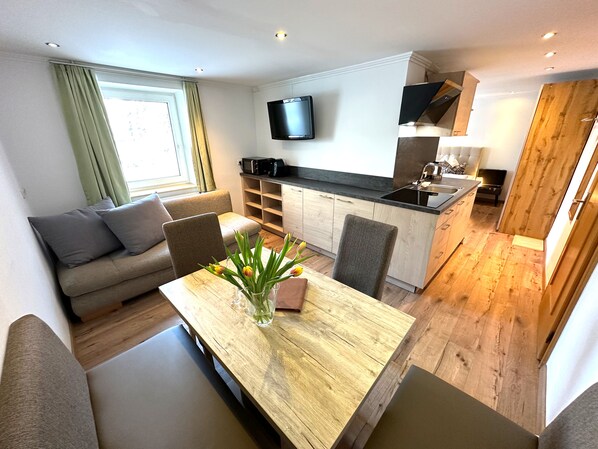 A modern living space with a sofa, dining table, and kitchen area. - GRUBERS Hotel Apartments Gastein (Bad Gastein)
