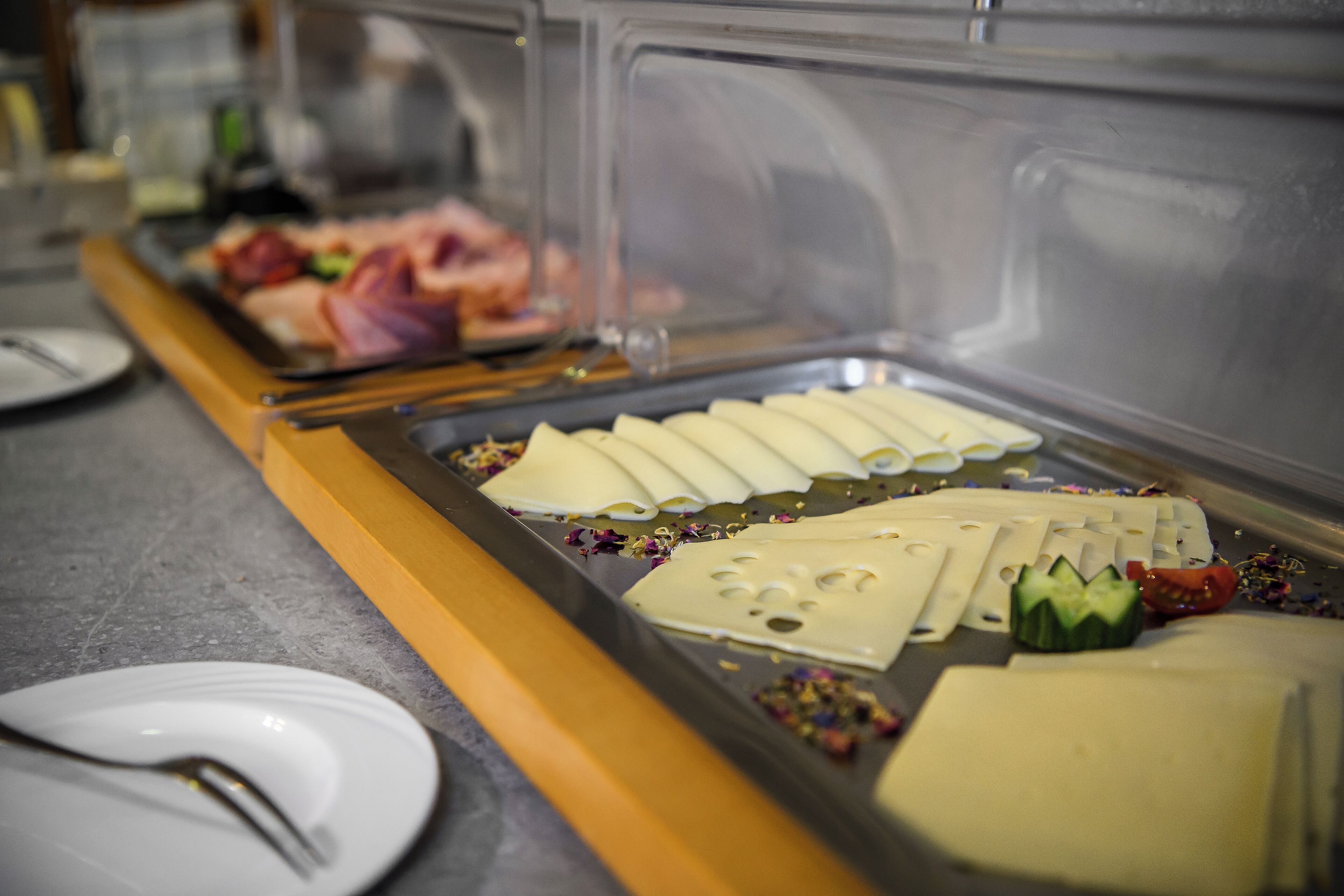 A buffet with various food items including sliced cheese, vegetables, and meats.