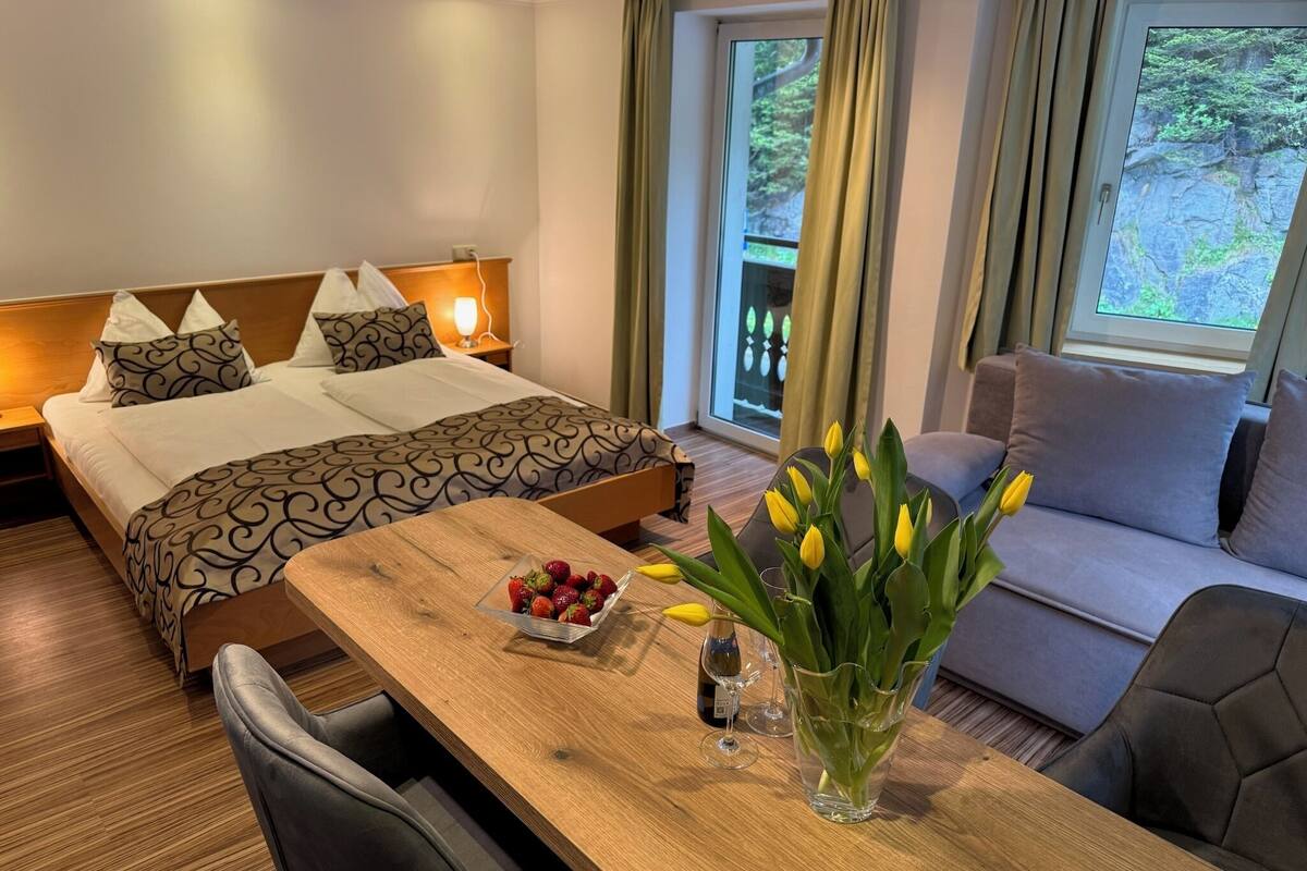 Habitació d'hotel amb un llit, una taula de fusta amb un bol de maduixes, un vas de tulipes i un sofà.
