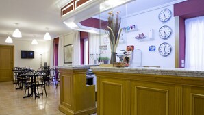 A hotel lobby with a reception desk, multiple clocks displaying different time zones, a dining area with chairs and tables, and a large window with curtains. - Boston (CORDOBA)