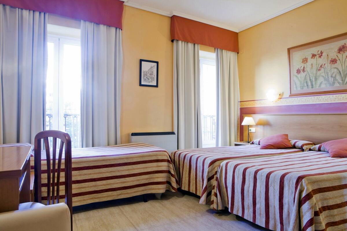 A hotel room with two beds, a desk, a chair, and a window with curtains.
