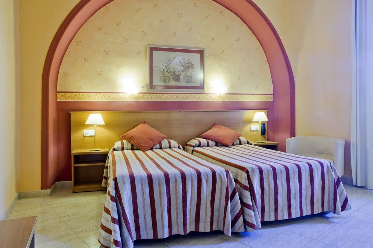 A hotel room with two beds, a wooden headboard, a framed picture, and bedside lamps.
