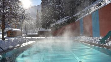Une piscine d’un bleu éclatant, entourée d’arbres couverts de neige, et un bâtiment à la façade rouge et bleue.