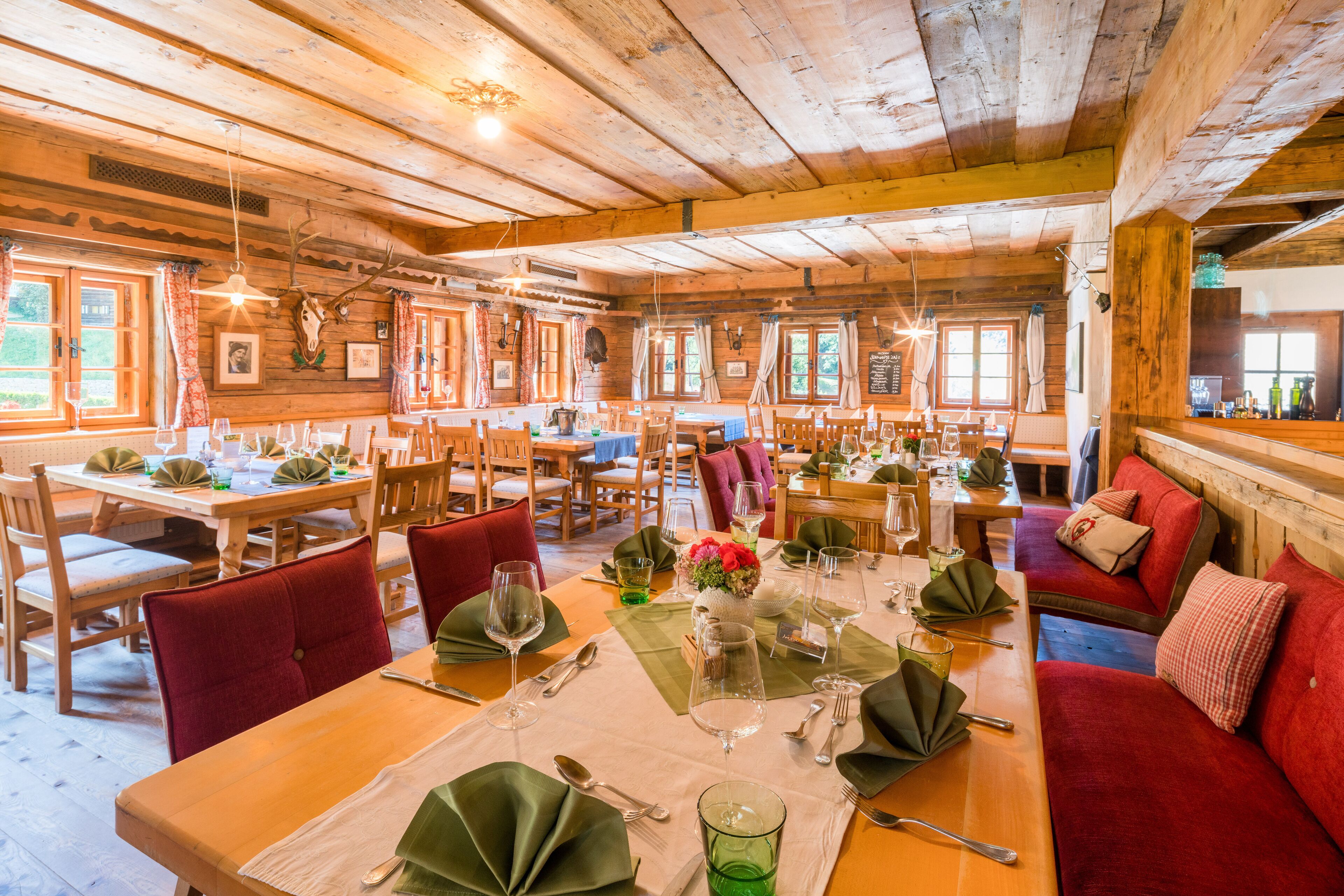 Een restaurant met houten inrichting, meerdere eettafels gedekt met groene servetten, wijnglazen en bestek.