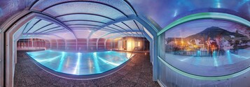 Una piscina interior moderna con techo curvo y paredes de vidrio, que ofrece vistas al exterior.
