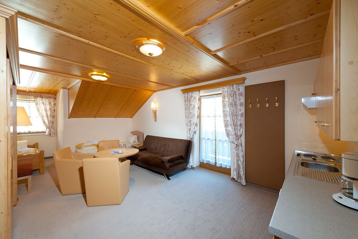Une pièce chaleureuse avec un plafond en bois, un canapé, une table à manger et un coin cuisine équipé d’un évier et d’une cuisinière.