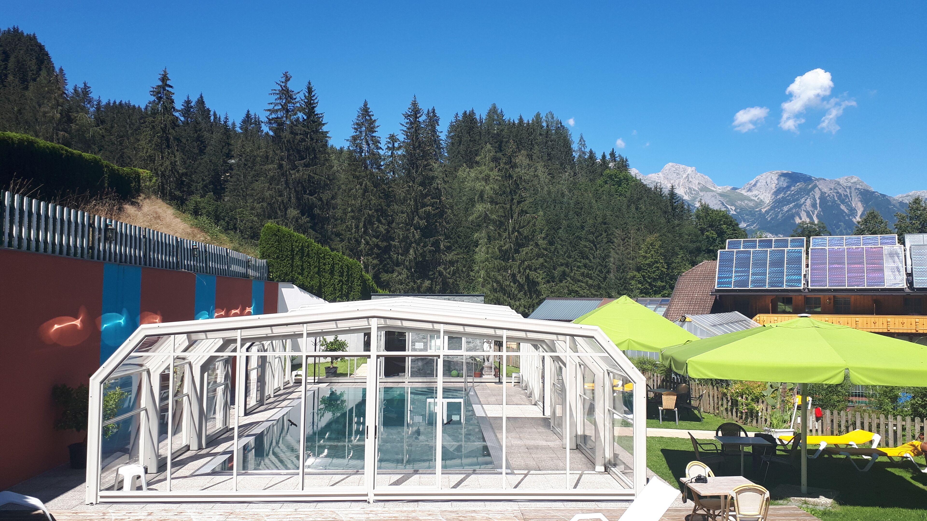 A glass-enclosed pool area with a view of a forest and mountains in the background.