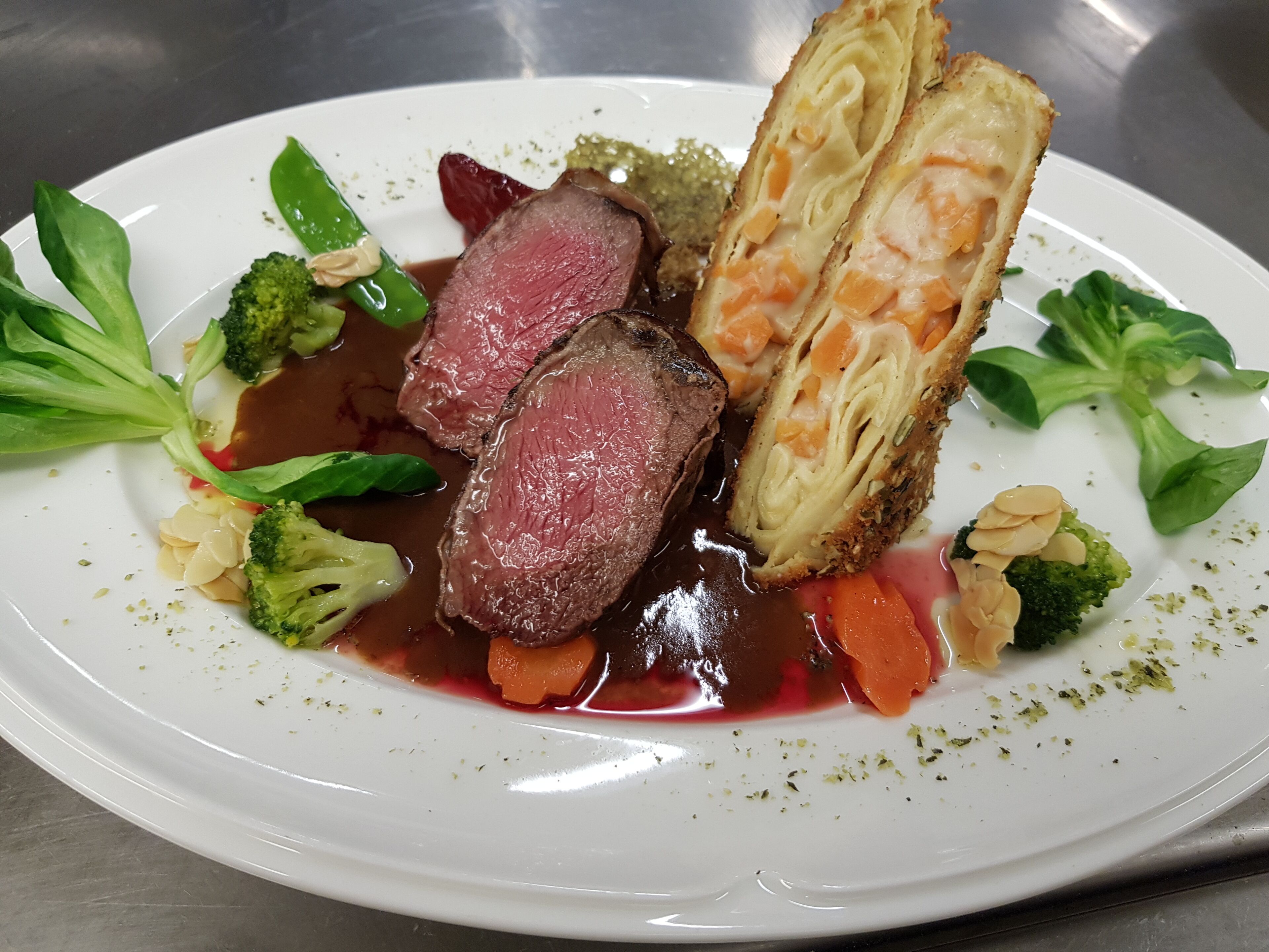 A white plate with a steak, vegetables, and a breaded item.