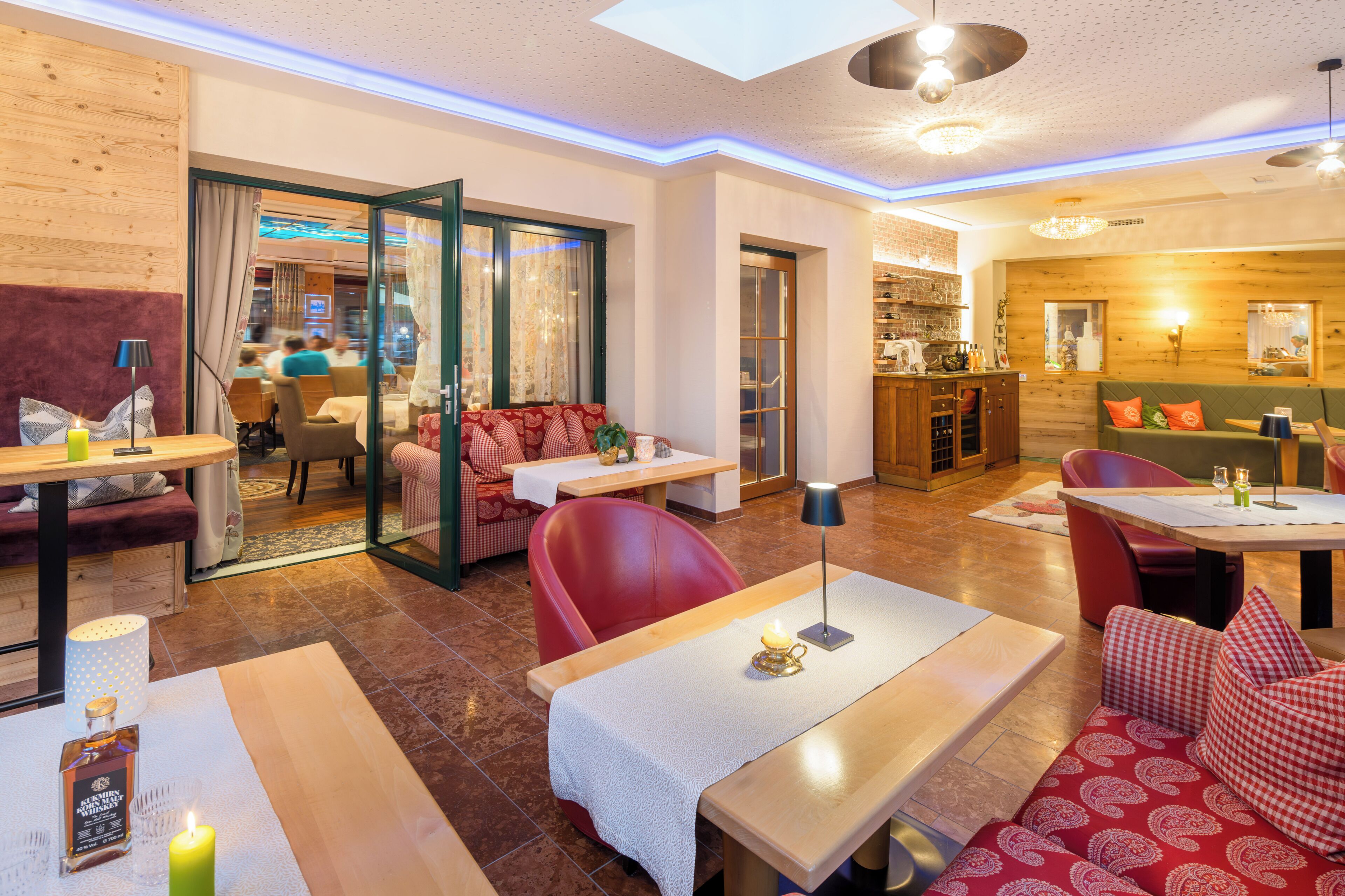 A modern hotel interior with a dining area, seating arrangements, and a visible kitchen.