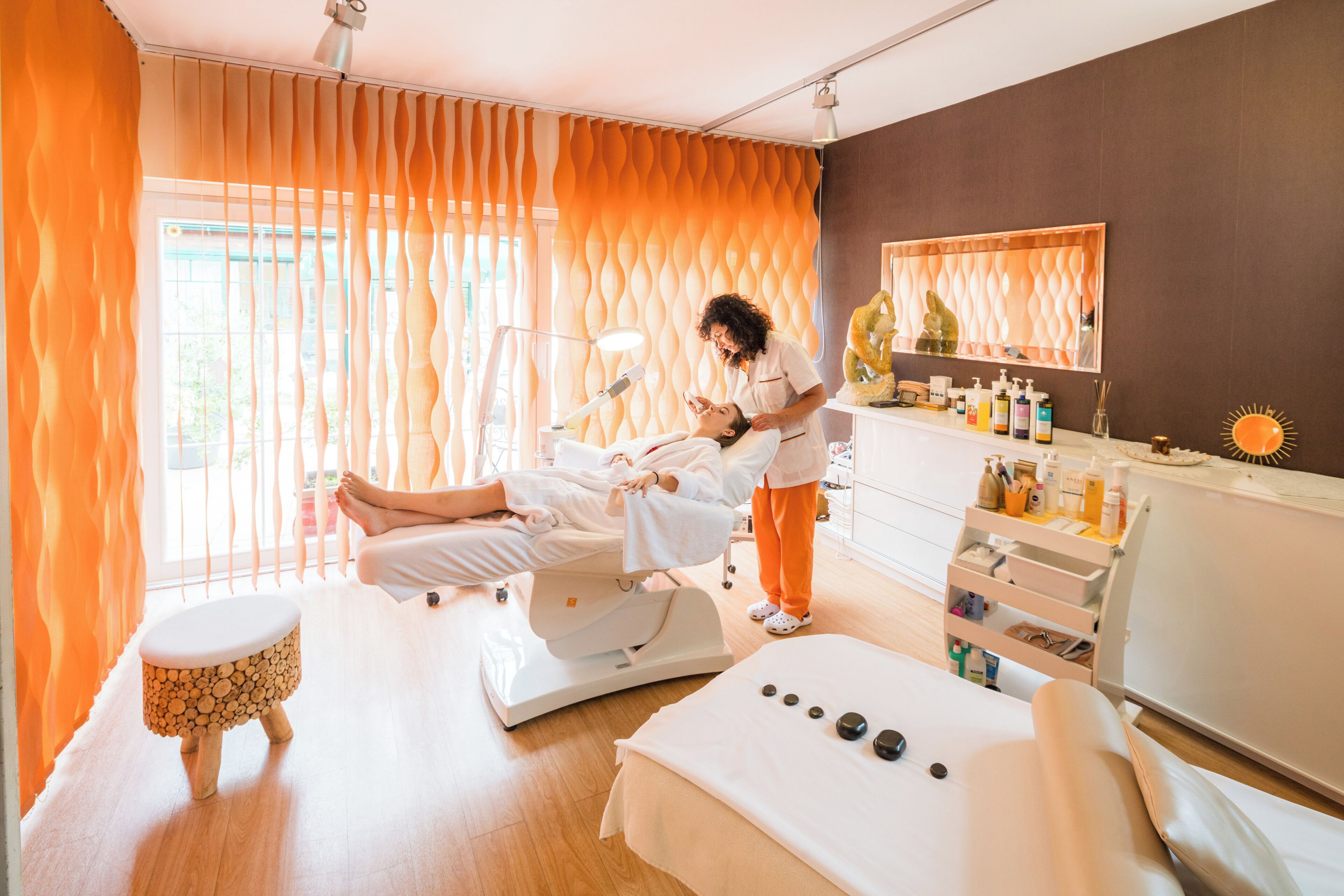 Ein Massageräum mit Massagetisch, einem kleinen Hocker und einem Regal mit Flaschen.