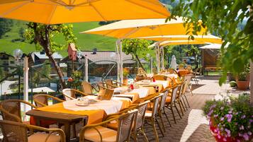 Un espace de restauration en plein air, avec des tables et des chaises placées sous des parasols jaunes, offrant une vue sur un paysage pittoresque.