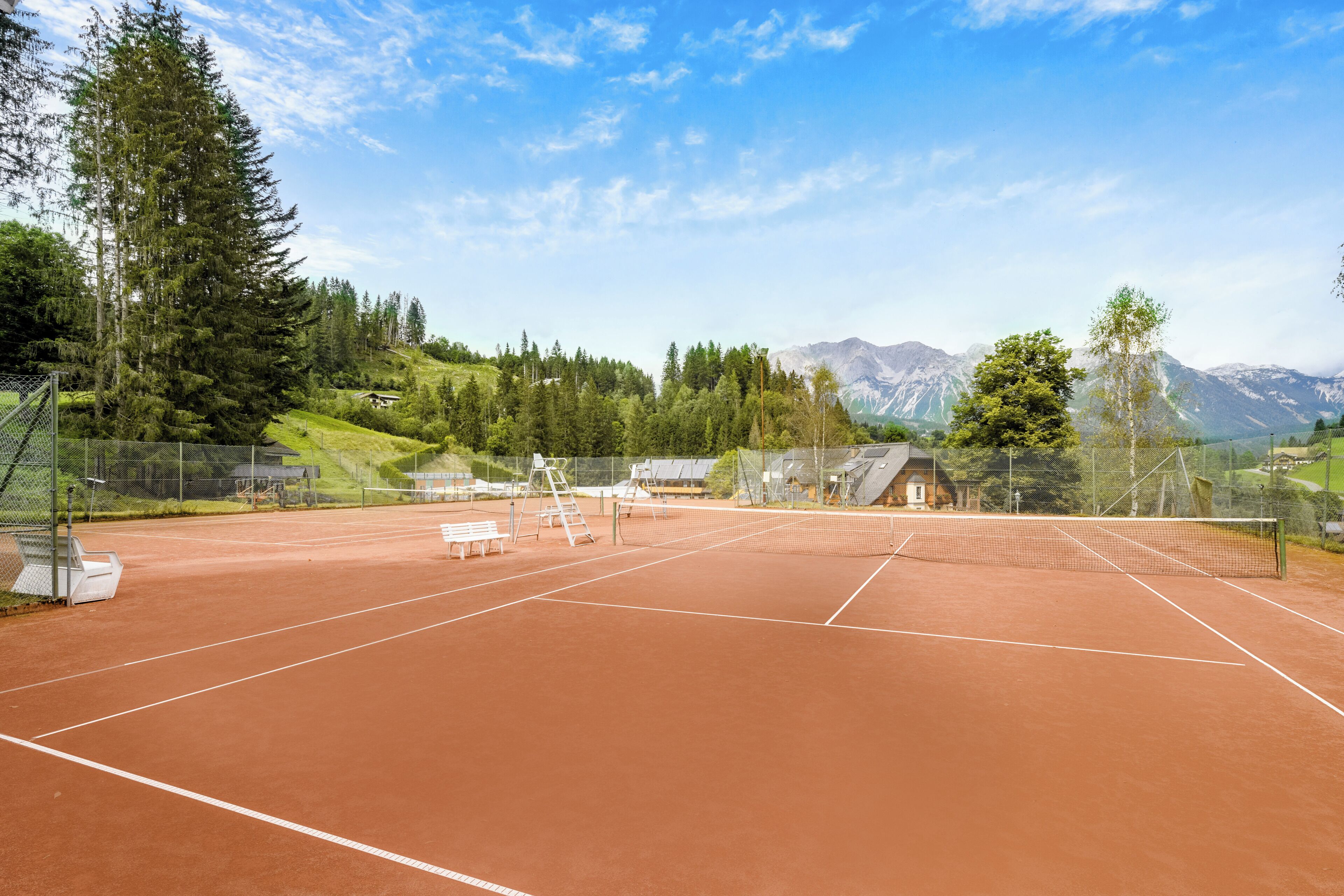 Una cancha de tenis con red, bancos y una valla.
