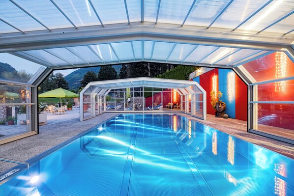 Piscina con cerramiento de vidrio, rodeada de mobiliario exterior y vistas a la montaña.