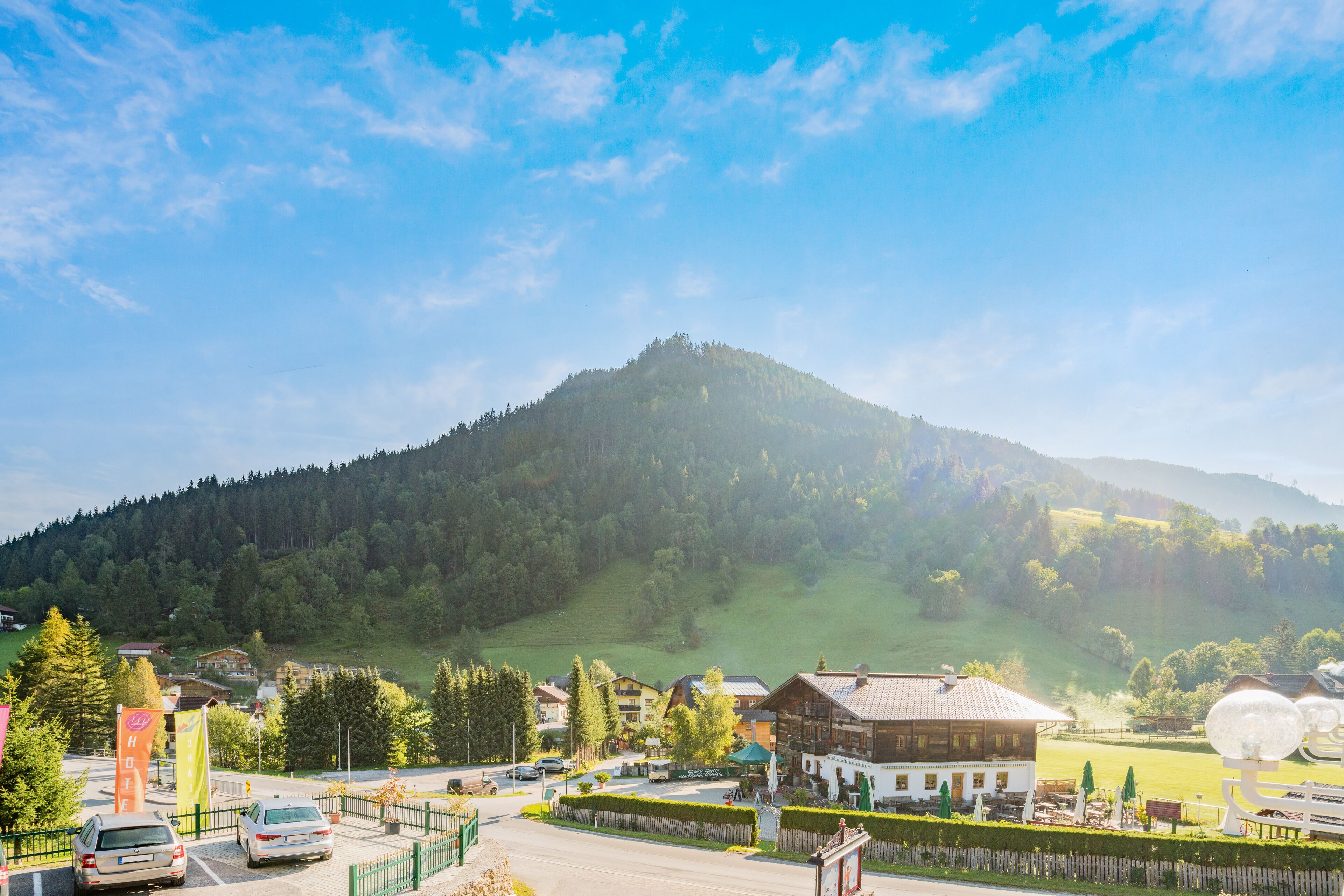Une montagne avec une colline boisée, un parking rempli de voitures et des bâtiments à l’architecture traditionnelle.