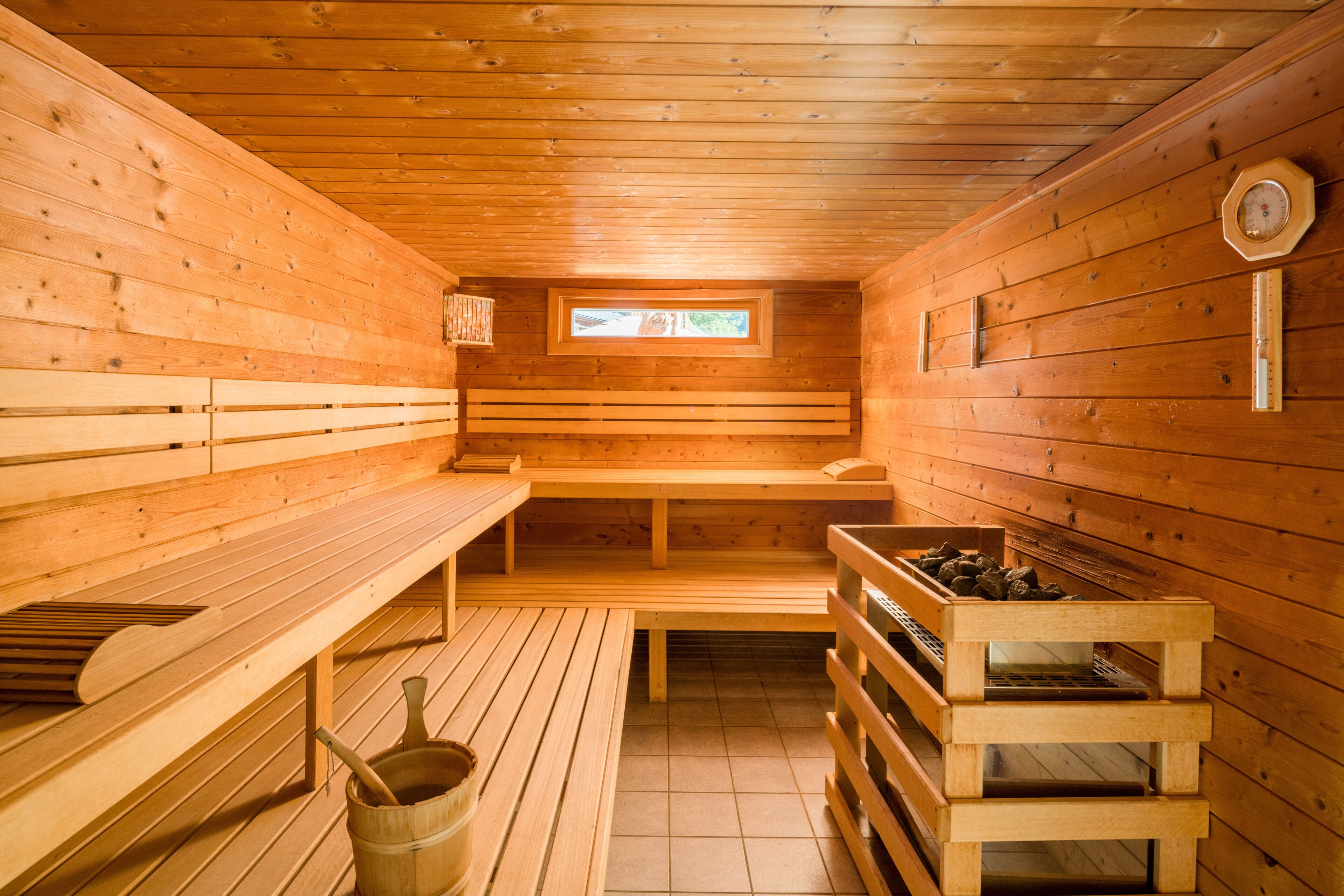 Una sauna de madera con bancos, una ventana pequeña y un balde de madera.